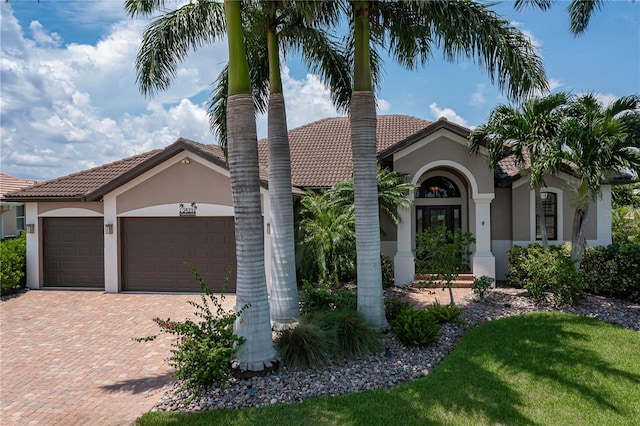 mediterranean / spanish home with a garage, decorative driveway, a tiled roof, and stucco siding