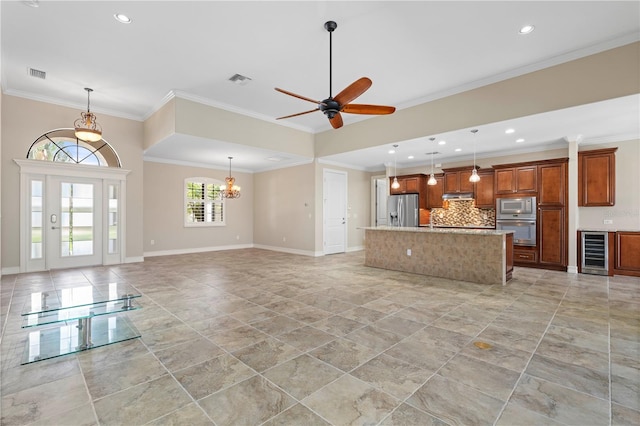 unfurnished living room with ceiling fan with notable chandelier, light tile patterned floors, wine cooler, sink, and ornamental molding