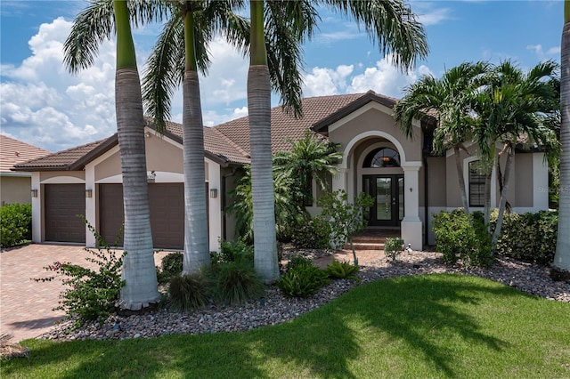 view of front facade with a garage, a tiled roof, decorative driveway, stucco siding, and a front yard