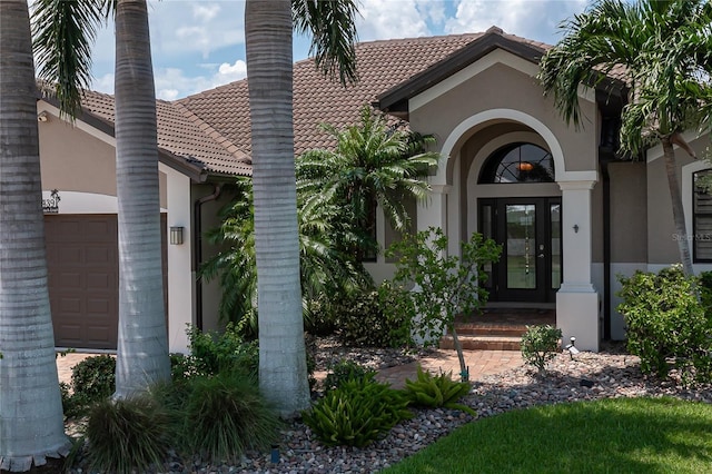 property entrance featuring a garage, stucco siding, a tiled roof, and french doors