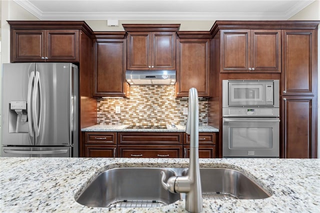 kitchen with under cabinet range hood, stainless steel appliances, a sink, ornamental molding, and backsplash