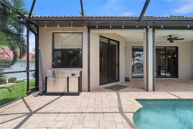 rear view of property featuring ceiling fan, glass enclosure, and a patio area