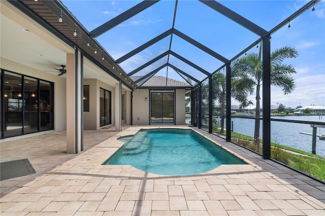 view of pool featuring glass enclosure, a water view, a patio area, and ceiling fan