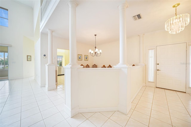 foyer entrance featuring ornate columns, a notable chandelier, a high ceiling, and light tile patterned floors