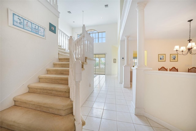 stairs with a towering ceiling, tile patterned flooring, an inviting chandelier, and decorative columns