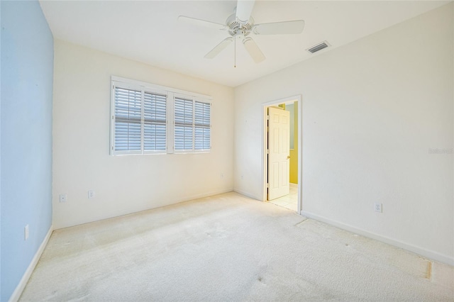 spare room featuring light colored carpet, ceiling fan, visible vents, and baseboards