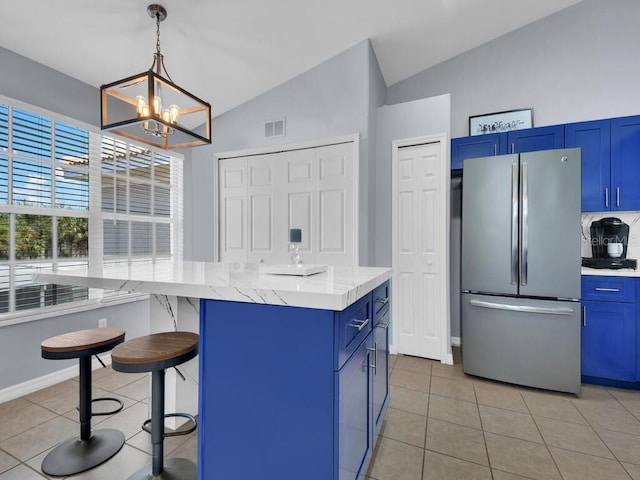 kitchen with a breakfast bar area, stainless steel fridge, vaulted ceiling, light tile patterned flooring, and blue cabinets