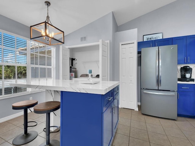 kitchen with stainless steel refrigerator, vaulted ceiling, blue cabinets, a breakfast bar, and light tile patterned floors