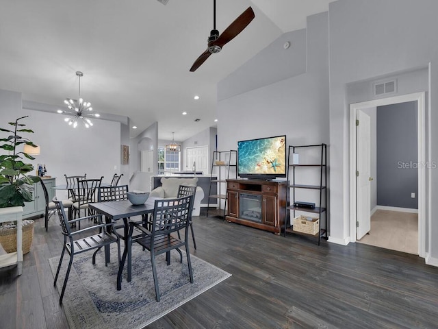 dining space with ceiling fan with notable chandelier, hardwood / wood-style flooring, and high vaulted ceiling