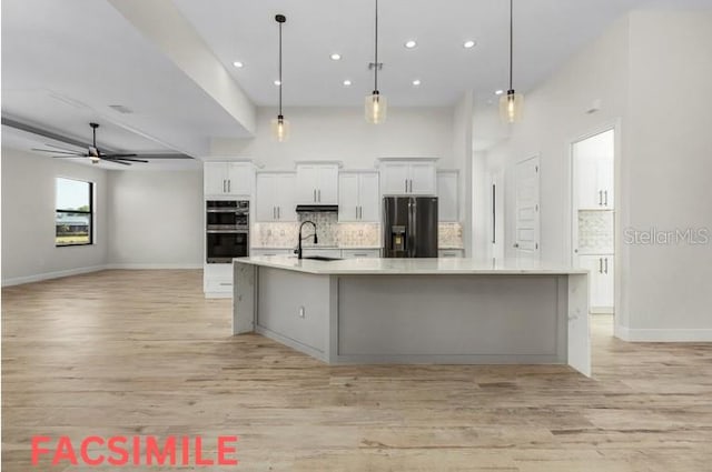 kitchen with decorative backsplash, light hardwood / wood-style flooring, double oven, a large island with sink, and black fridge