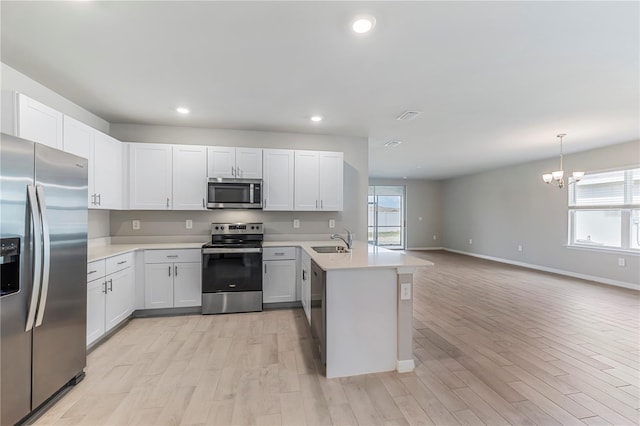 kitchen featuring white cabinets, appliances with stainless steel finishes, open floor plan, light countertops, and a sink