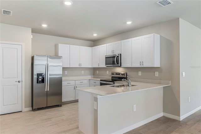 kitchen with a peninsula, visible vents, white cabinets, light countertops, and appliances with stainless steel finishes