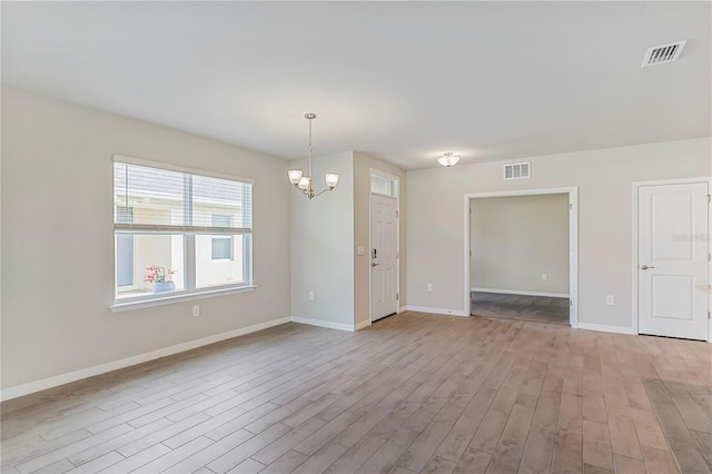 empty room featuring light wood-style floors, baseboards, visible vents, and a chandelier