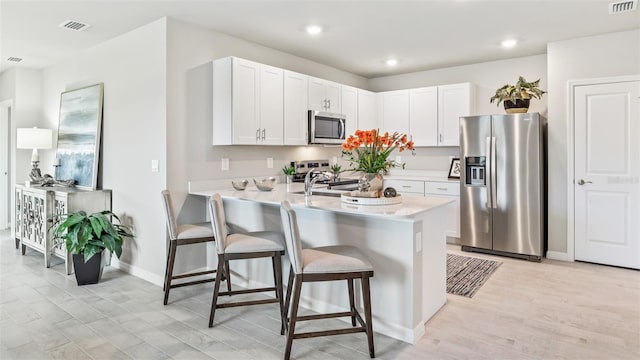 kitchen with stainless steel appliances, visible vents, white cabinets, light countertops, and a kitchen bar