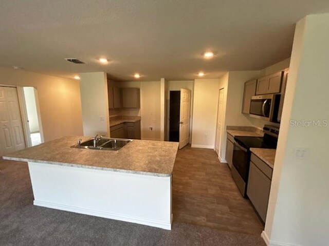 kitchen with appliances with stainless steel finishes, sink, an island with sink, and dark colored carpet