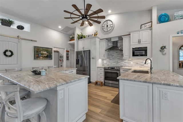 kitchen with appliances with stainless steel finishes, a spacious island, sink, wall chimney range hood, and ceiling fan