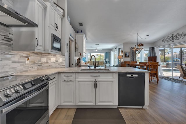 kitchen with wall chimney range hood, hardwood / wood-style flooring, backsplash, sink, and black appliances