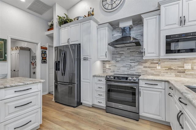 kitchen with appliances with stainless steel finishes, light hardwood / wood-style floors, decorative backsplash, white cabinetry, and wall chimney exhaust hood