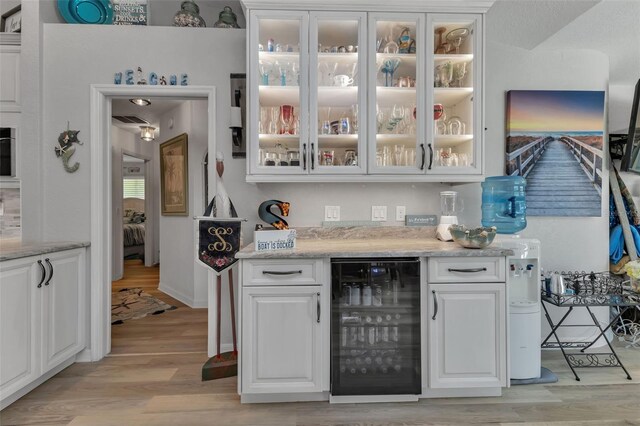 bar with light hardwood / wood-style flooring, white cabinetry, beverage cooler, and light stone countertops