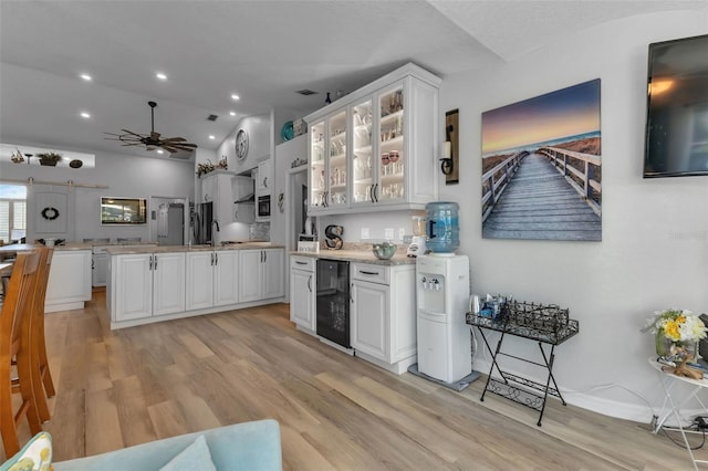 kitchen with light hardwood / wood-style floors, vaulted ceiling, wine cooler, white cabinets, and ceiling fan