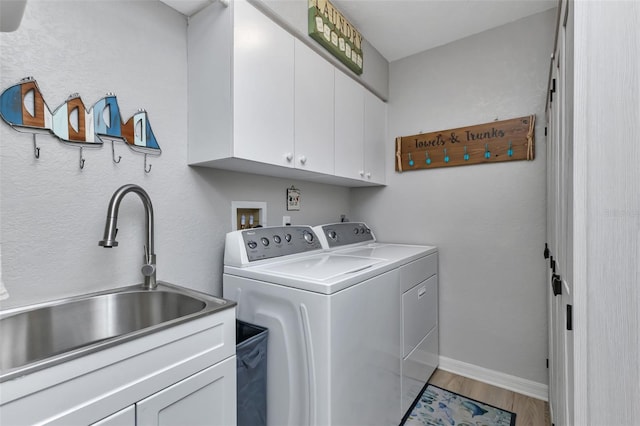 clothes washing area with sink, cabinets, light wood-type flooring, and washer and dryer