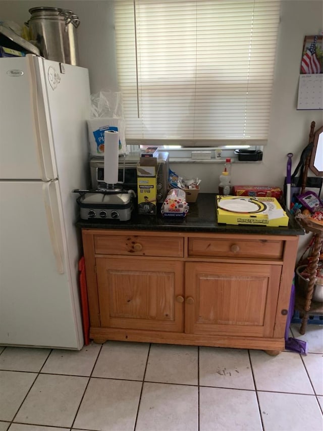 kitchen with freestanding refrigerator, brown cabinets, dark countertops, and light tile patterned floors