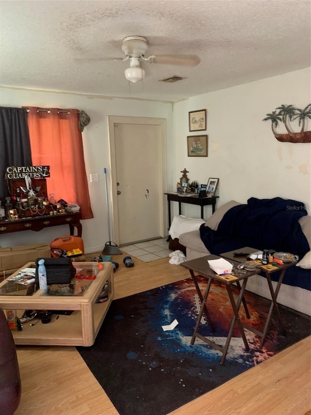 living room featuring ceiling fan, wood finished floors, visible vents, and a textured ceiling