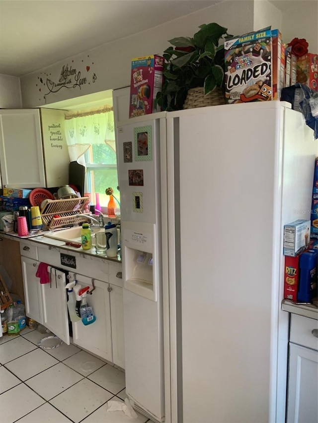 kitchen with white fridge with ice dispenser, white cabinets, a sink, and light tile patterned floors