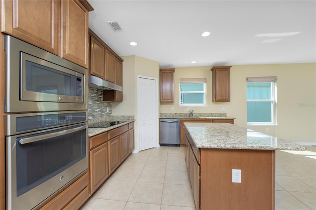 kitchen featuring stainless steel appliances, sink, light stone counters, light tile patterned floors, and a kitchen island