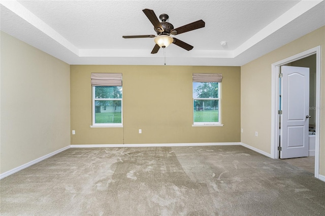 carpeted spare room with ceiling fan, a textured ceiling, and a tray ceiling