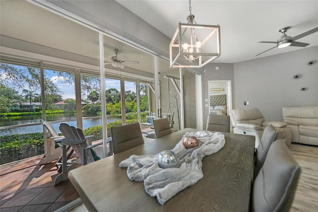 dining area featuring ceiling fan with notable chandelier, light hardwood / wood-style flooring, and a water view