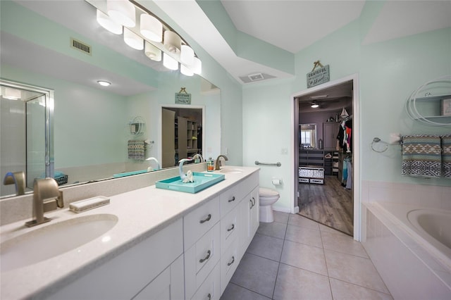 bathroom with a relaxing tiled tub, vanity, toilet, and tile patterned flooring