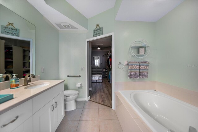 bathroom with toilet, tile patterned floors, tiled bath, and vanity