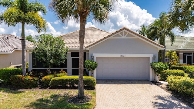 view of front facade featuring an attached garage, a tile roof, decorative driveway, and stucco siding