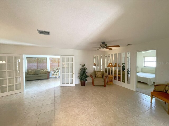 living area with ceiling fan, french doors, light tile patterned floors, and a textured ceiling