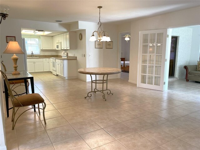 kitchen featuring white appliances, sink, light tile patterned floors, a chandelier, and white cabinetry