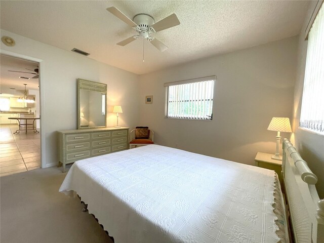 bedroom with ceiling fan, light colored carpet, and a textured ceiling