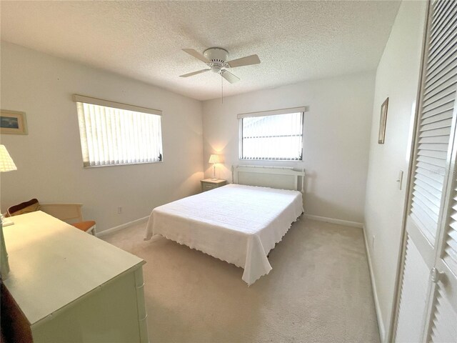 bedroom with a textured ceiling, light colored carpet, and ceiling fan