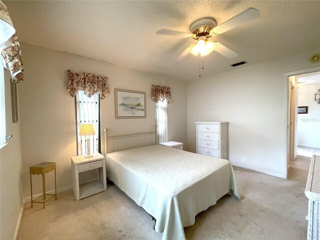 bedroom featuring ceiling fan, light colored carpet, and a textured ceiling