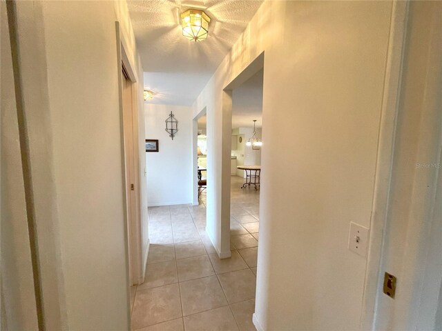 hall featuring light tile patterned floors, a textured ceiling, and an inviting chandelier