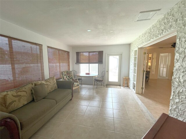 living room with ceiling fan, light tile patterned flooring, and a textured ceiling