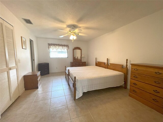 bedroom featuring ceiling fan, light tile patterned flooring, a textured ceiling, and a closet