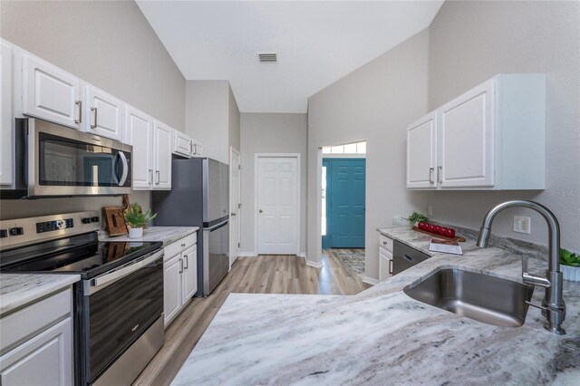 kitchen featuring stainless steel appliances, white cabinetry, light wood-type flooring, and light stone countertops