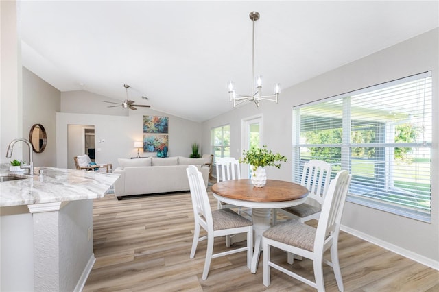 dining area featuring sink, light hardwood / wood-style floors, ceiling fan with notable chandelier, and vaulted ceiling