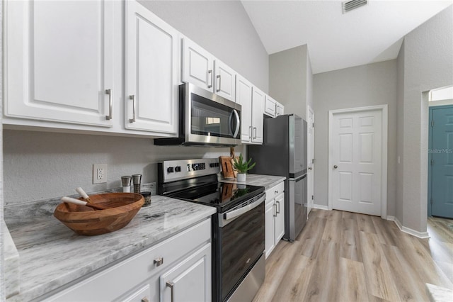 kitchen featuring white cabinetry, appliances with stainless steel finishes, light stone counters, light hardwood / wood-style floors, and lofted ceiling