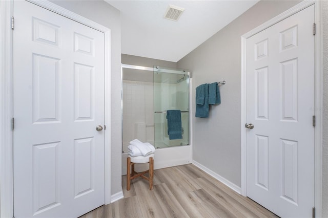 bathroom featuring wood-type flooring and shower / bath combination with glass door