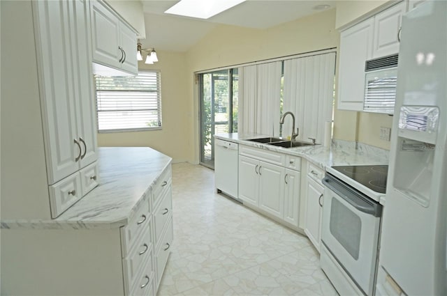 kitchen with lofted ceiling with skylight, white cabinetry, white appliances, and light tile patterned floors