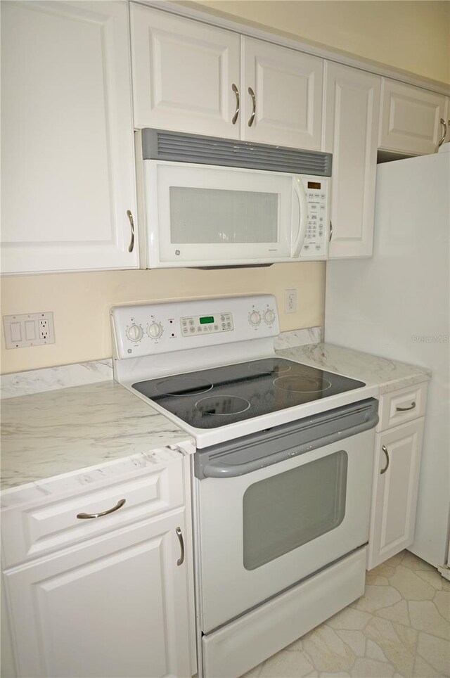 kitchen with white appliances, white cabinetry, and light tile patterned floors