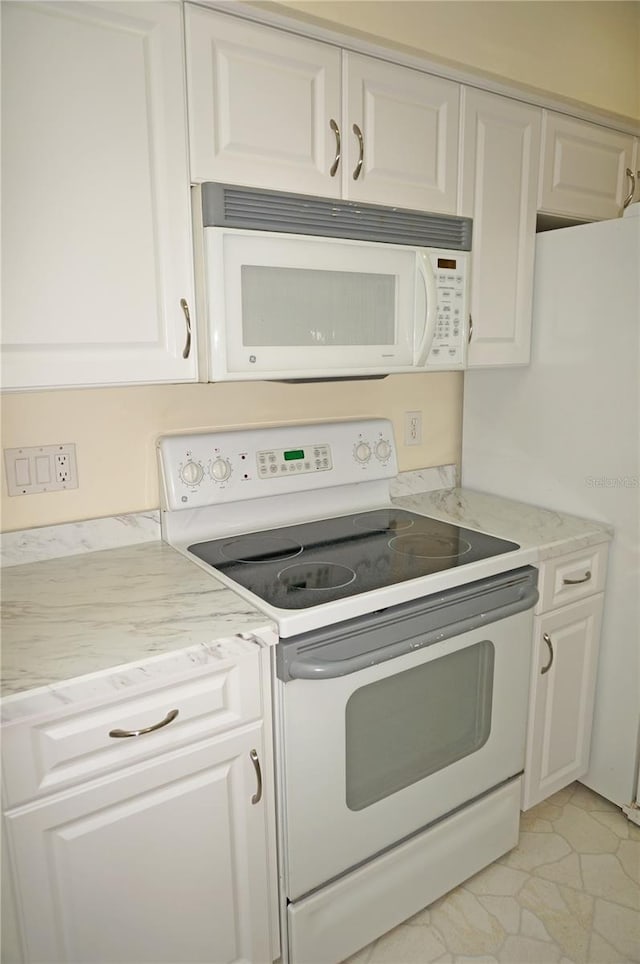 kitchen featuring white appliances, light stone counters, and white cabinets