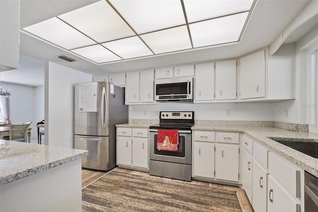 kitchen featuring appliances with stainless steel finishes, light stone counters, light hardwood / wood-style floors, and white cabinetry